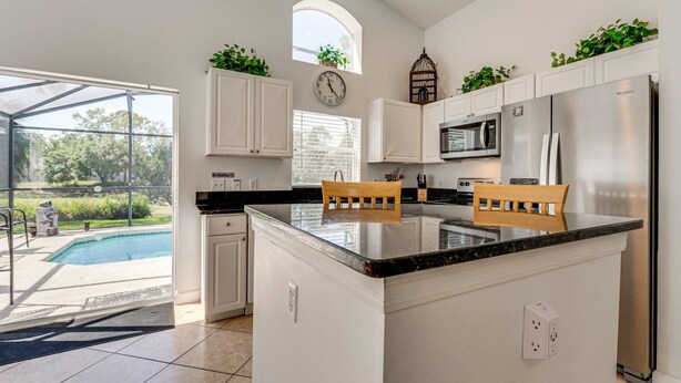 A modern kitchen with white cabinets, a central island with chairs, a built-in microwave, and a refrigerator. - Beautiful 3-bedroom house, with private pool, backing onto golf course (Haines City)