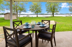 A covered patio with a table set for four, surrounded by chairs, overlooking a lake with boats and a dock. - Adorable Chapman Lake Front Home (Warsaw)