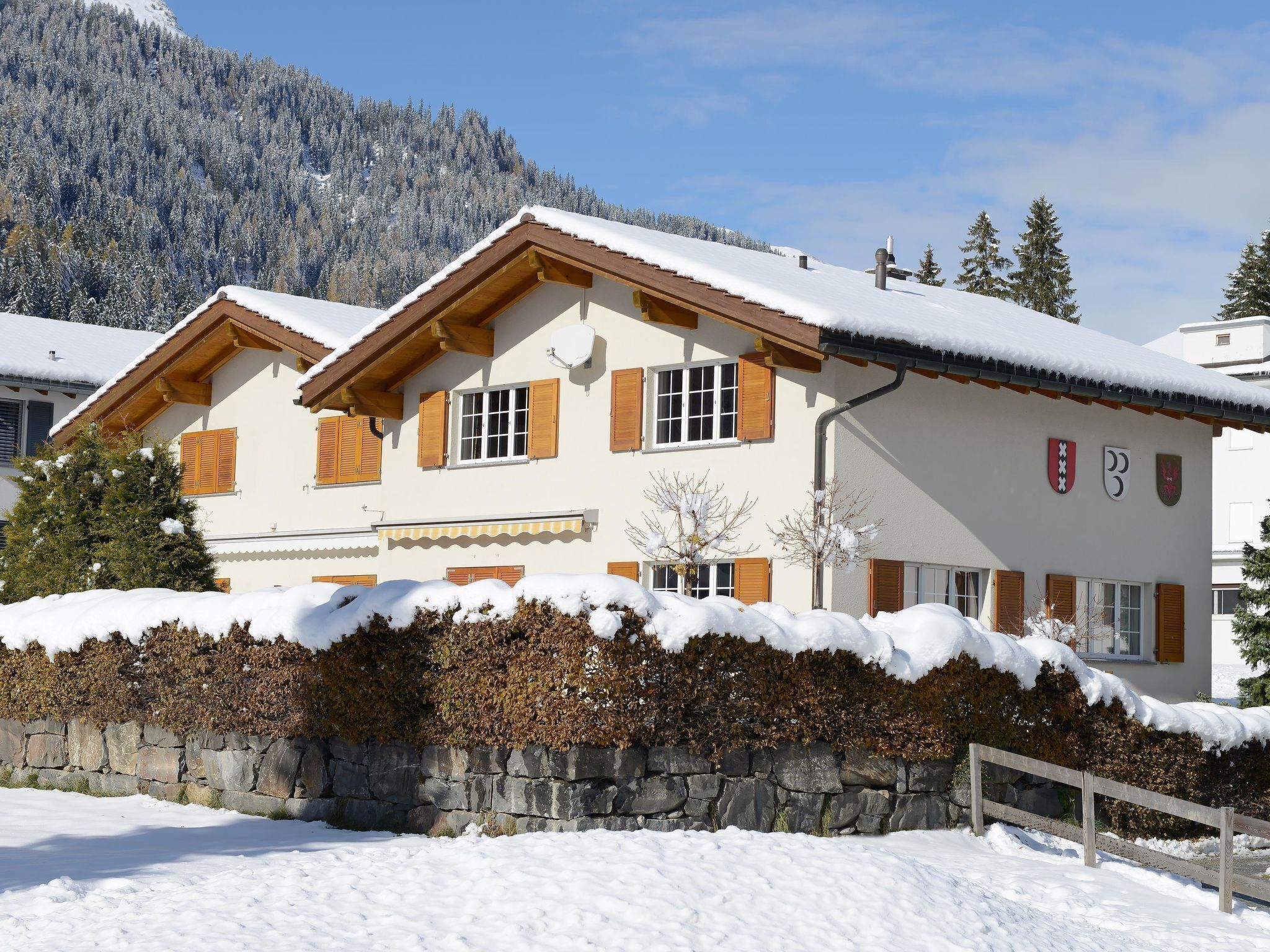 En traditionel schweizisk chalet med stenvæg og træpersienner, foran et sneklædt bjerglandskab.