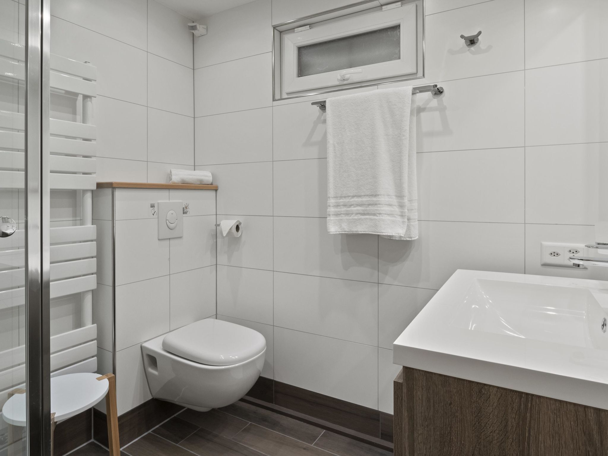 Moderni kylpyhuone, jossa on wc, pesuallas ja pyyhekoukku.