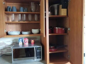 Uma cozinha com micro-ondas, prateleiras com pratos, tigelas e uma caixa de cereal.