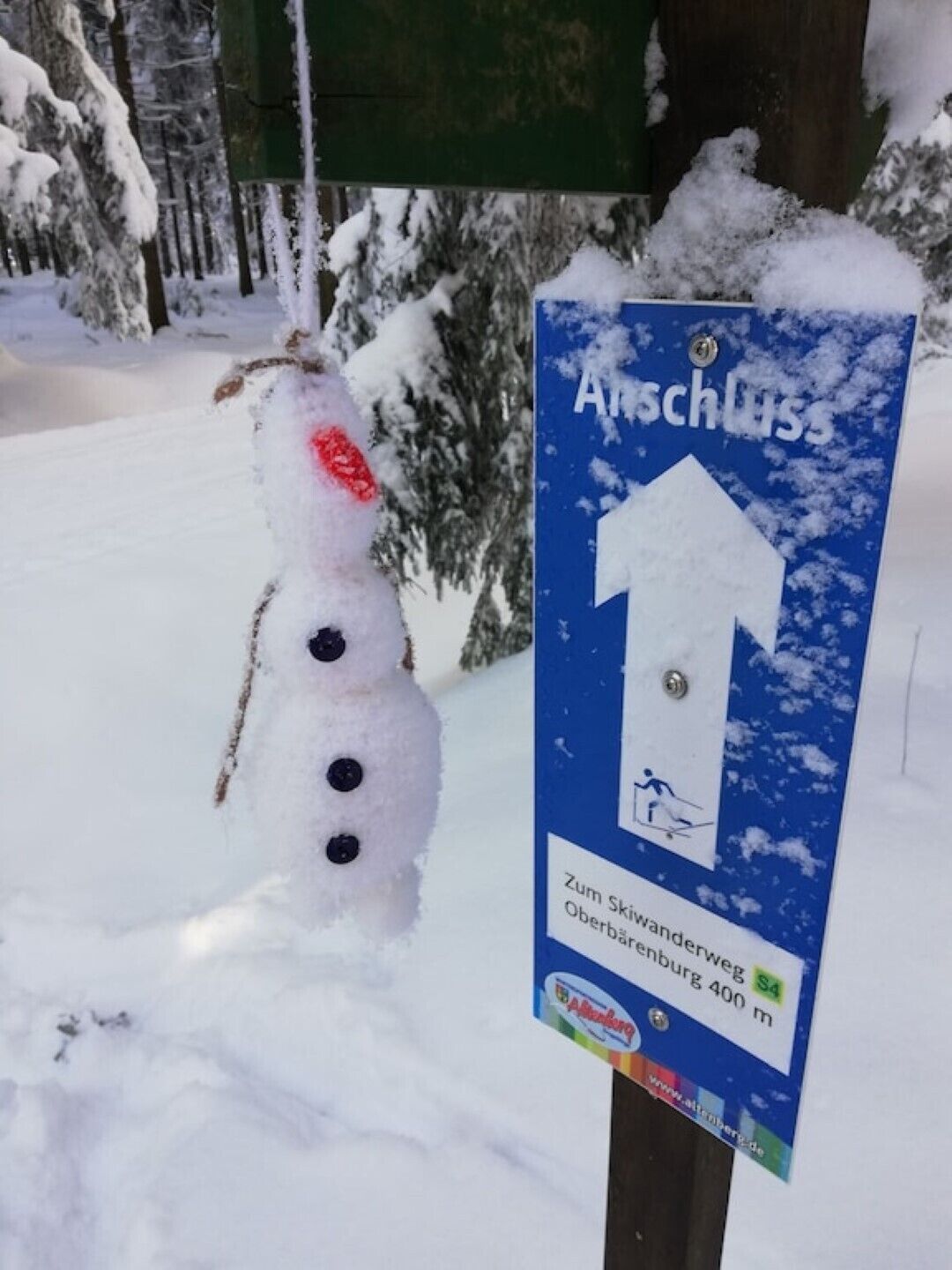 Un muñeco de nieve con un letrero a su lado. El letrero es azul con texto blanco y una flecha que apunta hacia arriba.