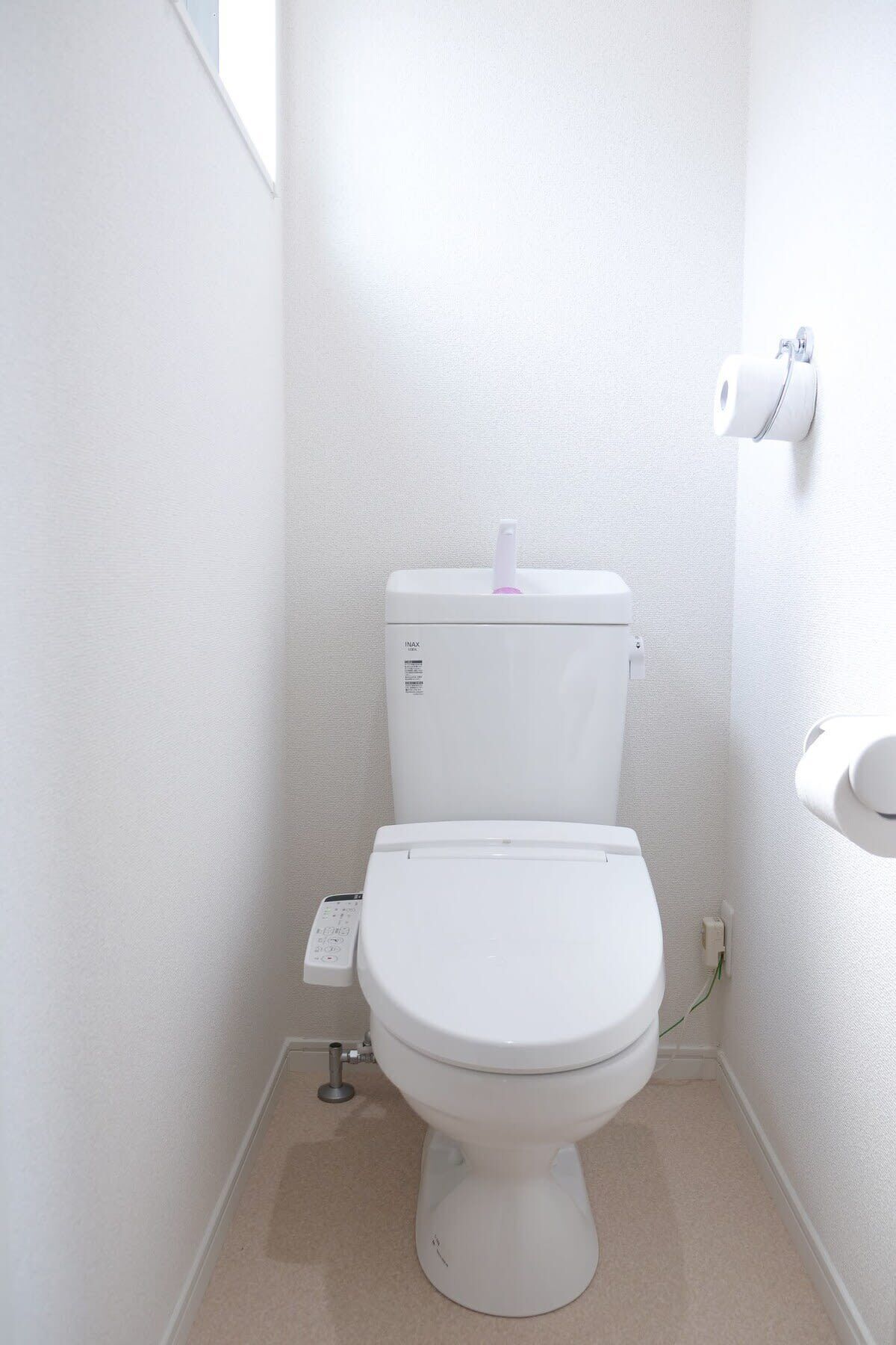 A small, white bathroom with a toilet, a bidet, and a toilet paper holder.