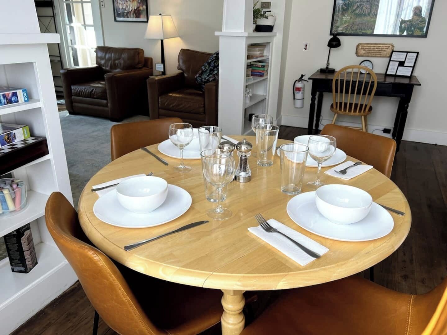Une table à manger dressée pour quatre personnes, avec de l’assiette et des bols blancs, ainsi que des verres transparents, entourée de chaises en cuir marron.