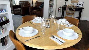 Une table à manger dressée pour quatre personnes, avec de l’assiette et des bols blancs, ainsi que des verres transparents, entourée de chaises en cuir marron.