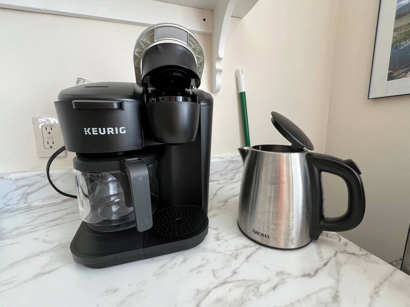 Une machine à café Keurig posée sur un comptoir en marbre, avec une tasse en acier inoxydable et une paille verte.