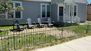 Una casa de dos pisos con un porche, patio trasero cercado y sillas Adirondack.