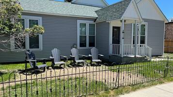 Une maison à deux étages avec un porche, une cour arrière clôturée et des fauteuils Adirondack.