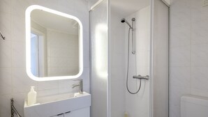 A modern bathroom with a white sink, a mirror, and a shower enclosure. - Greenhouse Apartments (Helgoland)