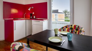 A modern kitchen with red walls, white cabinets, and a dining area with colorful chairs. - Greenhouse Apartments (Helgoland)