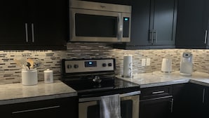 Una cucina moderna con mobili scuri, elettrodomestici in acciaio inossidabile e zanzariera piastrellata.