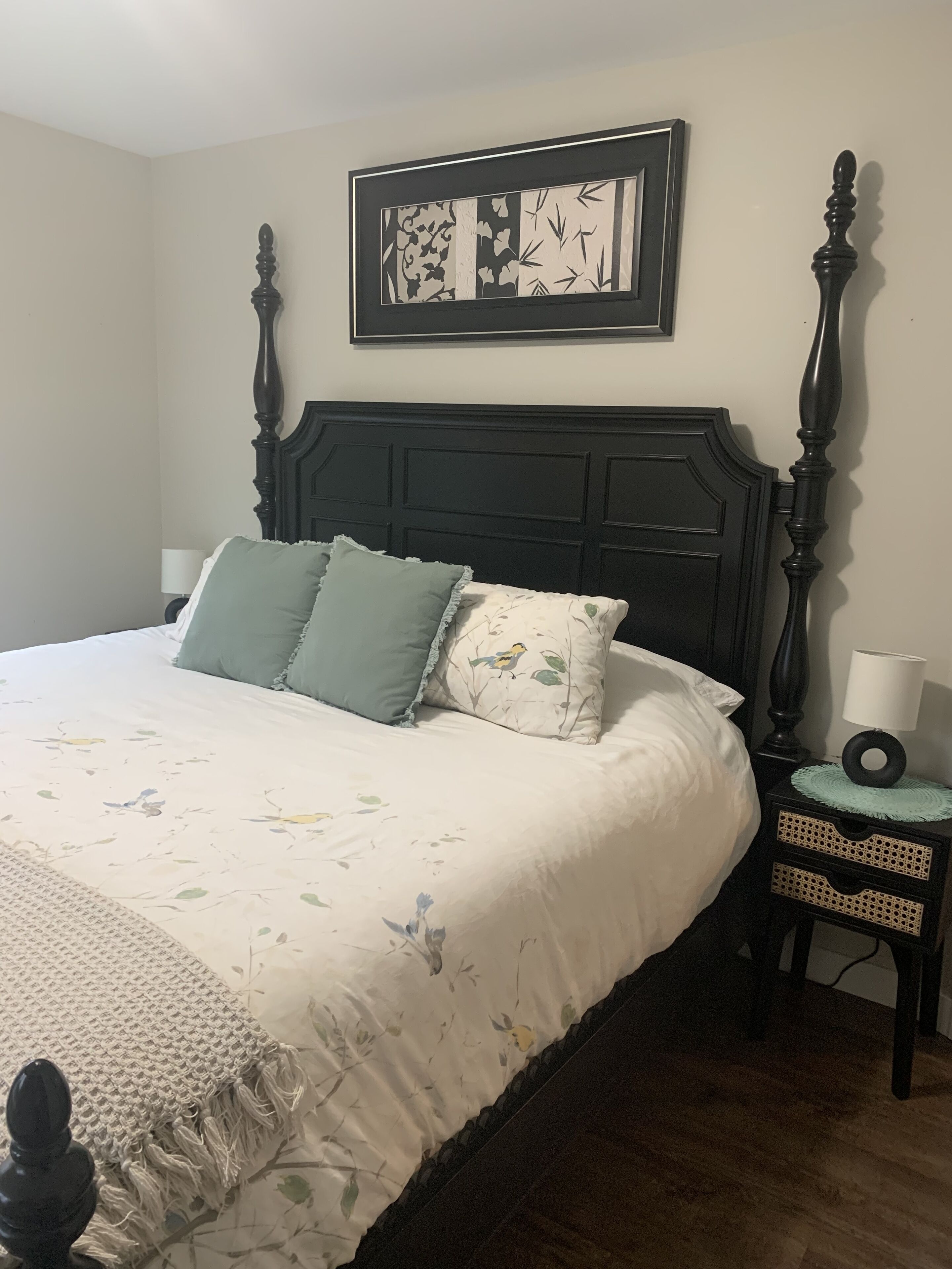 A bedroom with a large bed, a nightstand, a wall-mounted picture, and a wooden floor.