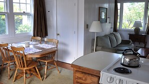 A kitchen with a wooden table, chairs, a stove, and a view of greenery outside. - Brant Point Courtyard (Nantucket)