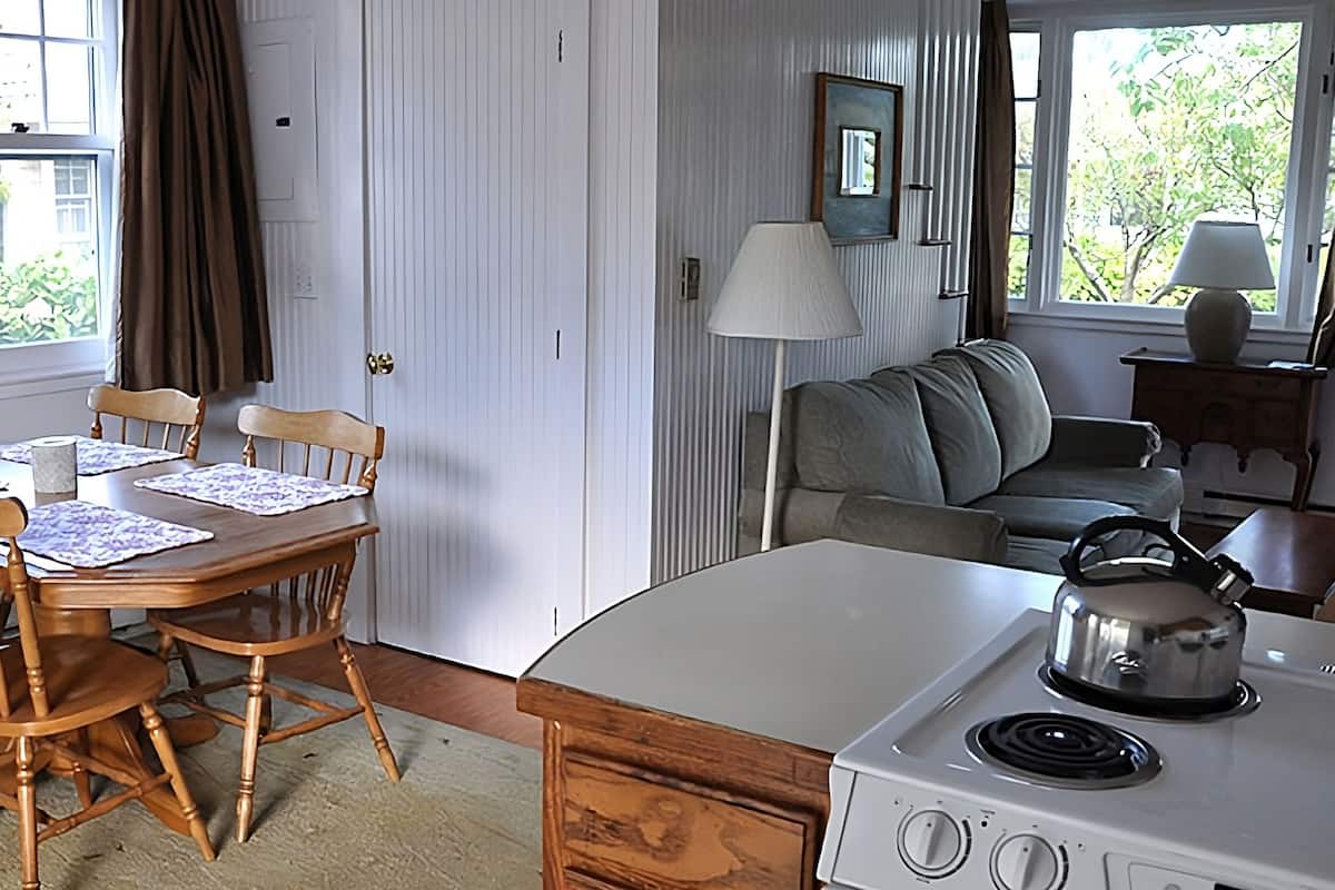 A kitchen with a wooden table, chairs, a stove, and a view of greenery outside.