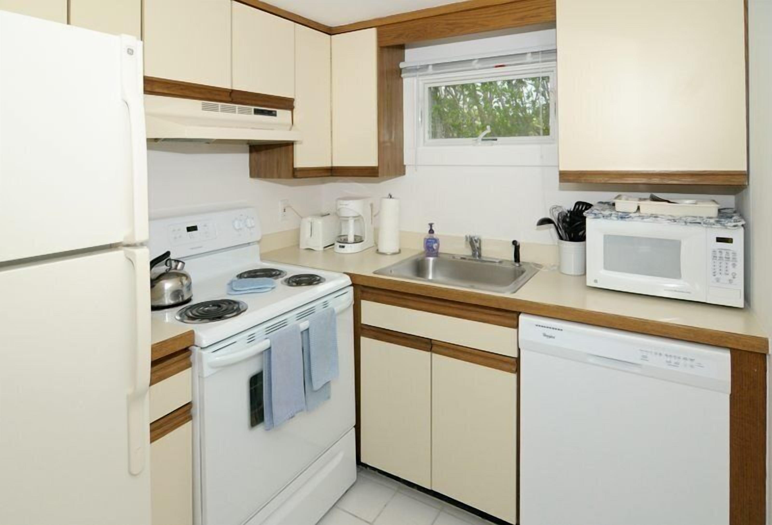 Une cuisine compacte équipée d’un réfrigérateur, d’une cuisinière, d’un four à micro-ondes, d’un évier et d’un lave-vaisselle.