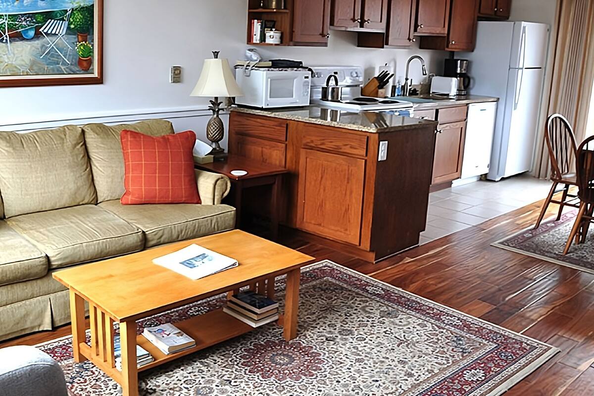 A cozy living room with a sofa, coffee table, and a kitchen area with wooden cabinets and a white refrigerator.