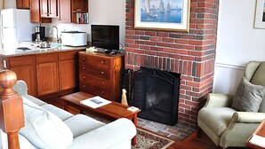 A living room with a fireplace, a television, wooden cabinets, and a sofa. - Brant Point Courtyard (Nantucket)