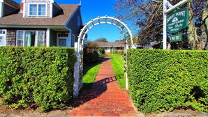 A pathway leading to a house with a white archway, surrounded by well-maintained hedges. - Brant Point Courtyard (Nantucket)