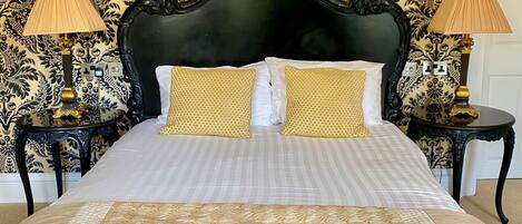 Una cama con cabecera negra, dos almohadas doradas y una colcha blanca.