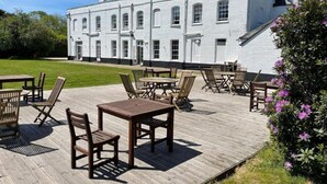 A white building with multiple windows and a wooden deck with tables and chairs. - The Retreat New Forest (Christchurch)