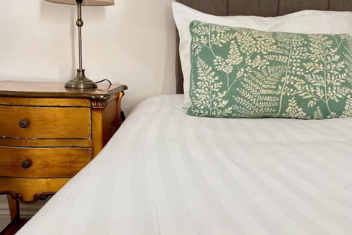 Cama bem arrumada com travesseiro estampado em verde e edredom branco.