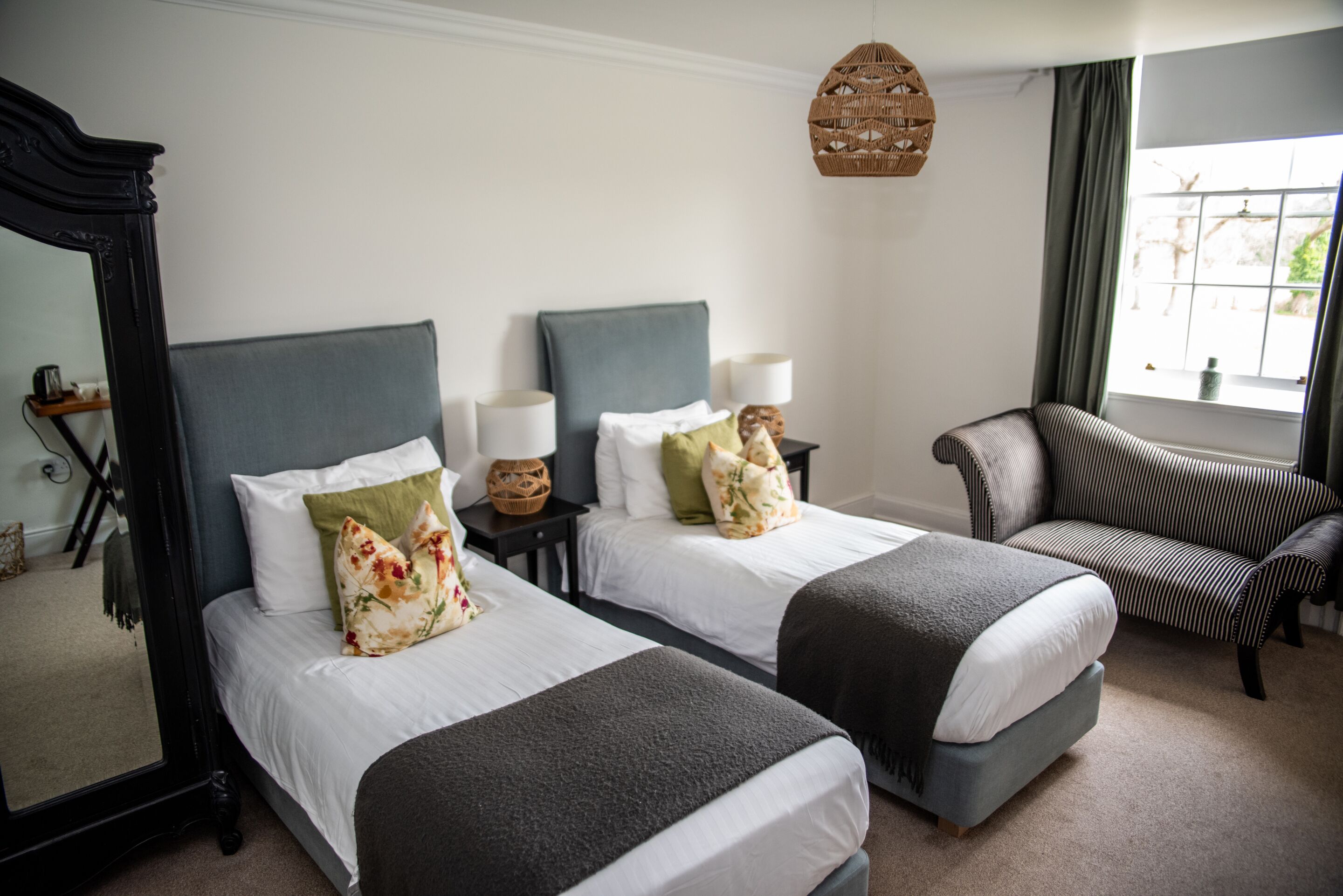 A hotel room with two beds, a large mirror, a hanging light, and a window with curtains.