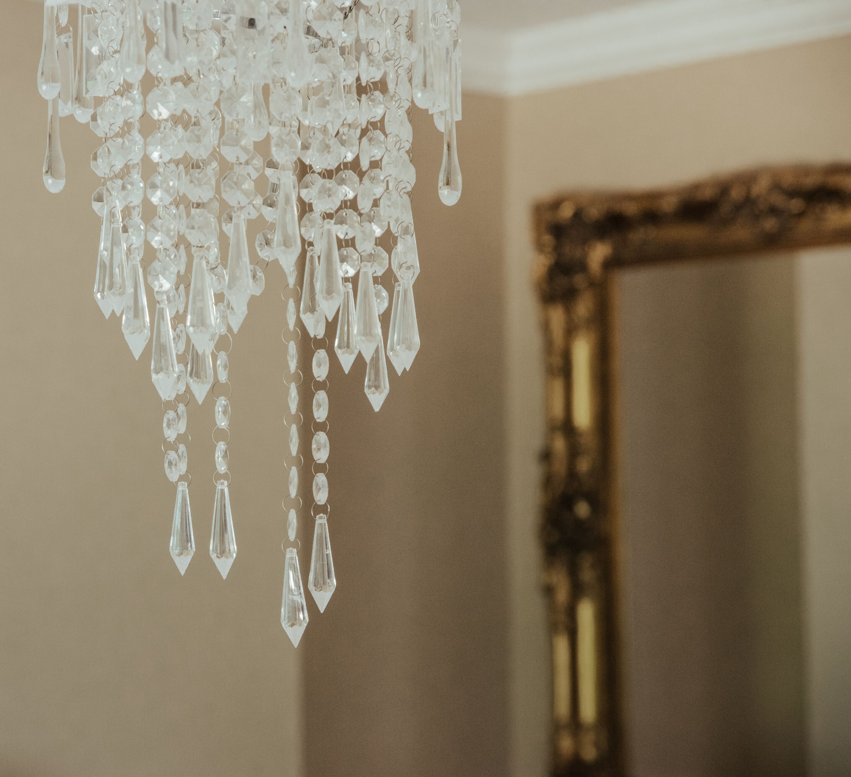 A chandelier with clear crystals hanging in a room with a gold-framed mirror.