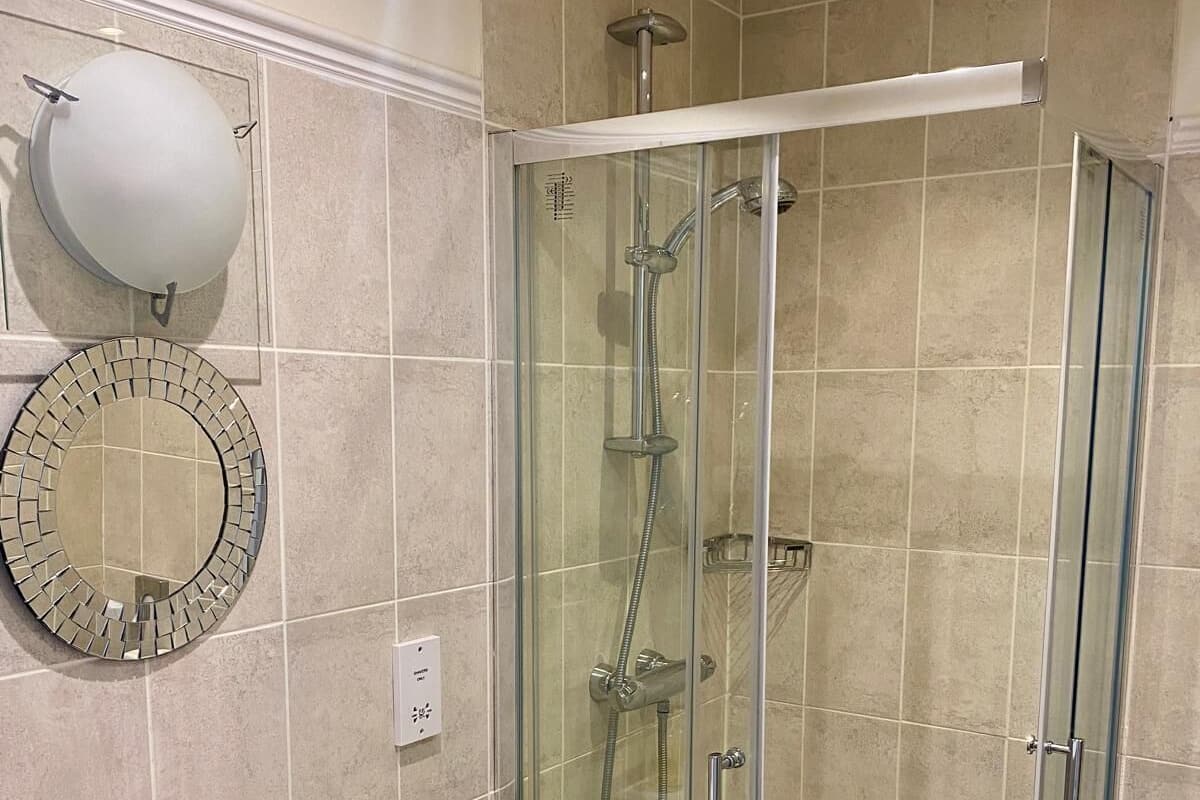 Ein Badezimmer mit Duschkabine, Waschbecken in Weiß und einem an der Wand befestigten Spiegel.