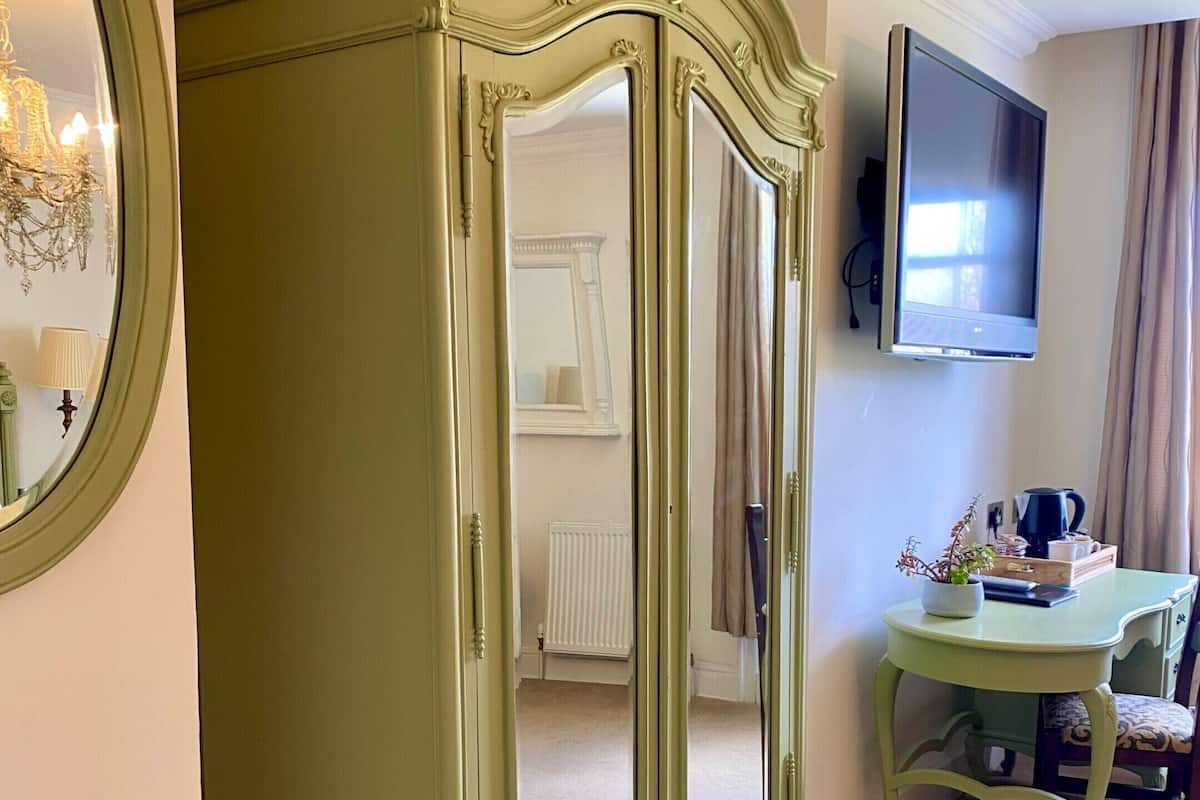 Ein Zimmer mit einem grünen Schrank, einem runden Spiegel, einem Fernseher, einem Tisch mit einer Pflanze und einem Stuhl.