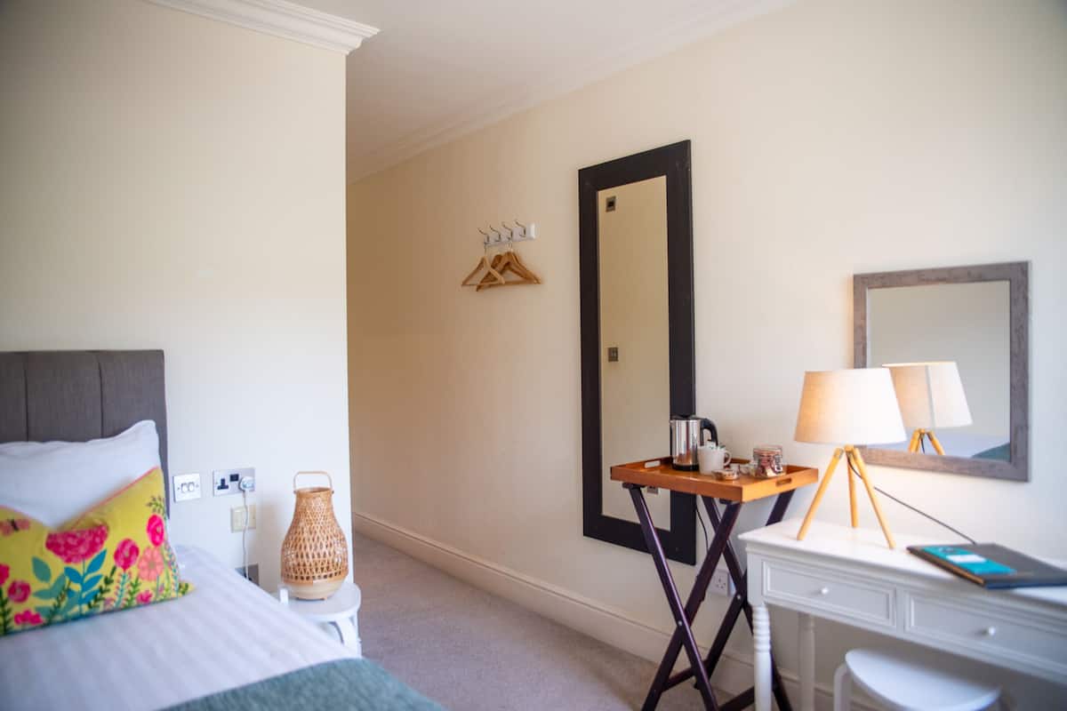 Ein Hotelzimmer mit Bett, Nachttisch, Lampe, Spiegel und einem Wandhaken für Kleidung.