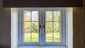 A window with white frames and two brass handles, overlooking a grassy area with trees. - The Retreat New Forest (Christchurch)