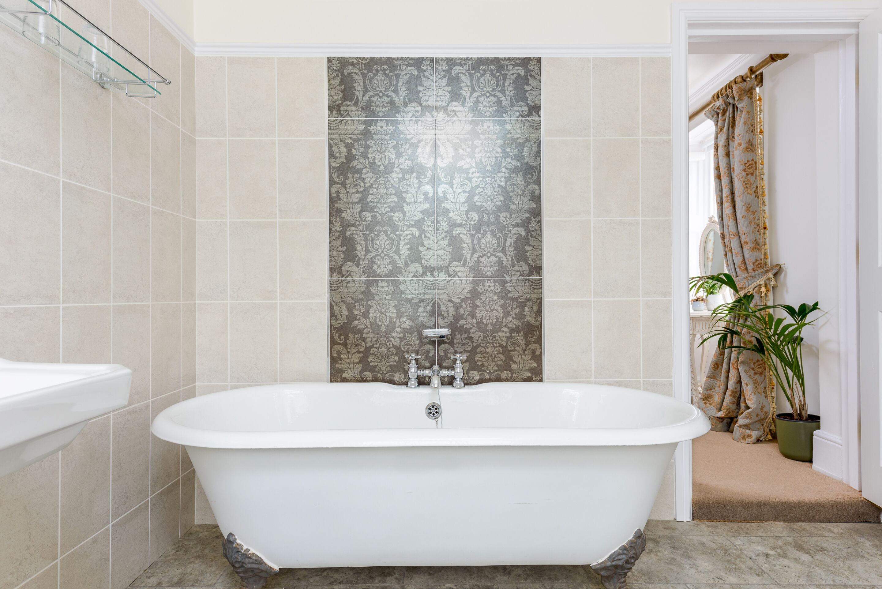 A bathroom with a freestanding bathtub, a glass shelf, and a patterned tile wall.