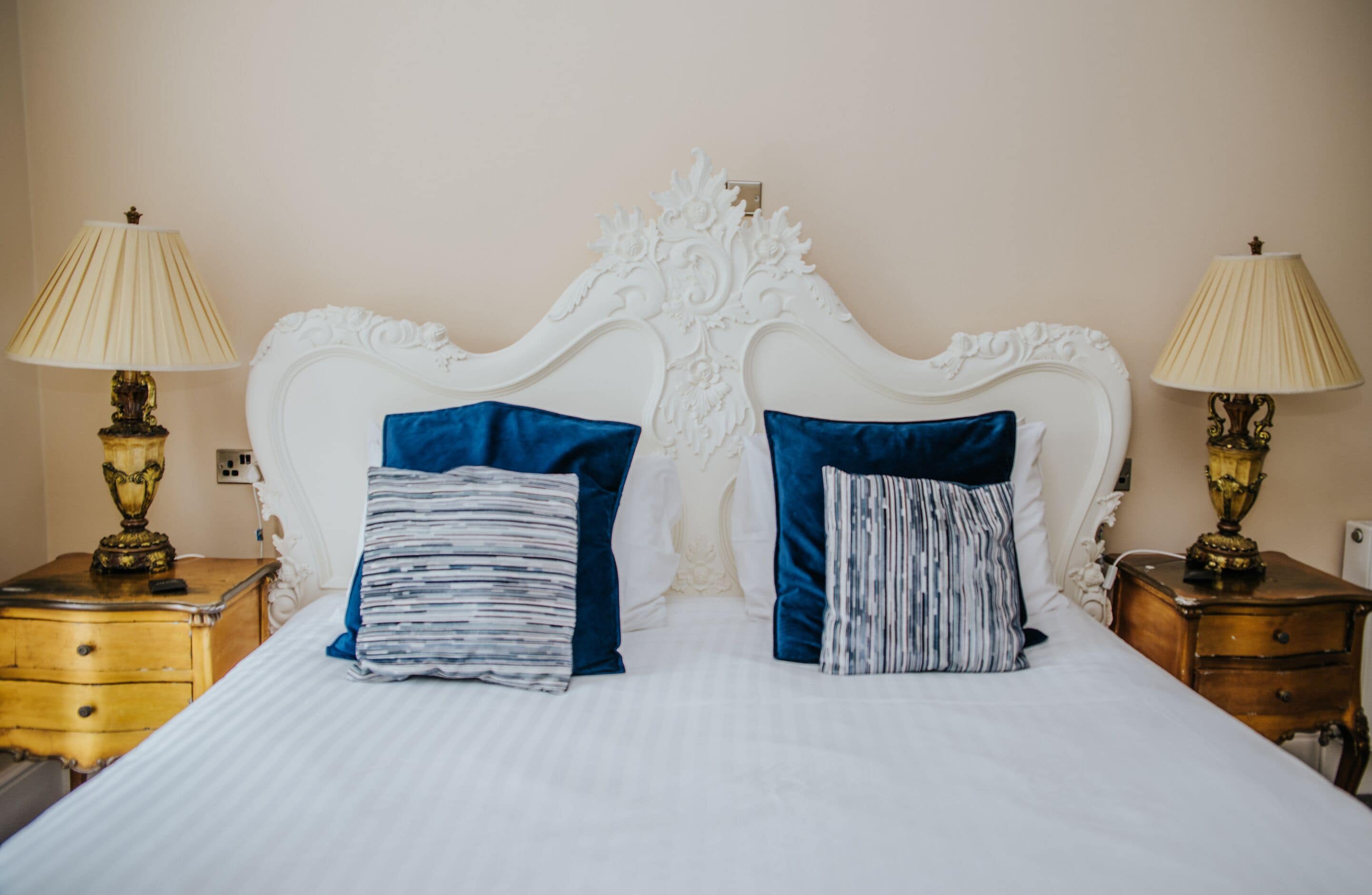 A bed with a white headboard, two blue pillows, and two bedside tables with lamps.