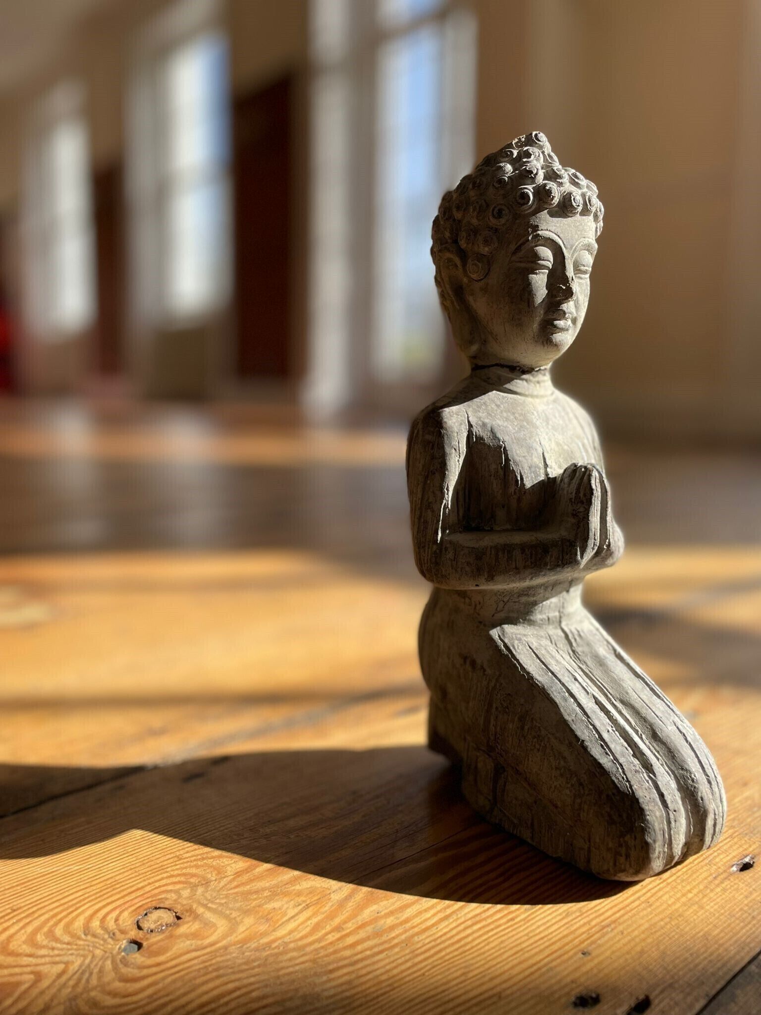 Una estatua de piedra de una figura sentada sobre un suelo de madera en un edificio con ventanas amplias.