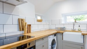 A modern kitchen with a built-in oven, a washing machine, and a window providing natural light. - The Retreat New Forest (Christchurch)