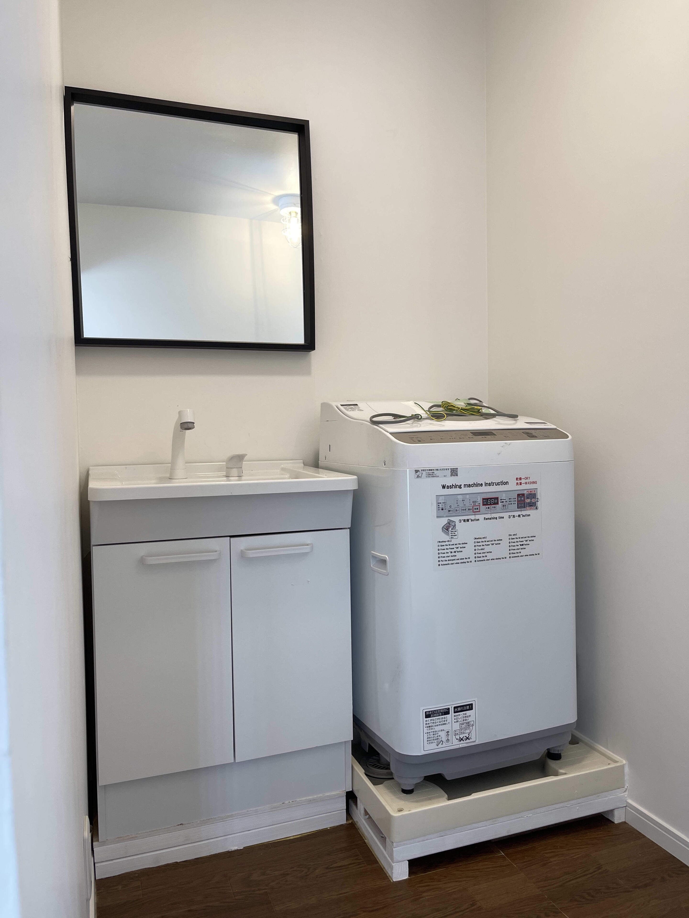 A small bathroom with a white sink, mirror, and white washing machine.