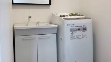 A small bathroom with a white sink, mirror, and white washing machine.