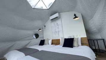 A cozy, uniquely shaped bedroom with a large bed, a bedside mirror, and a wall-mounted air conditioner.