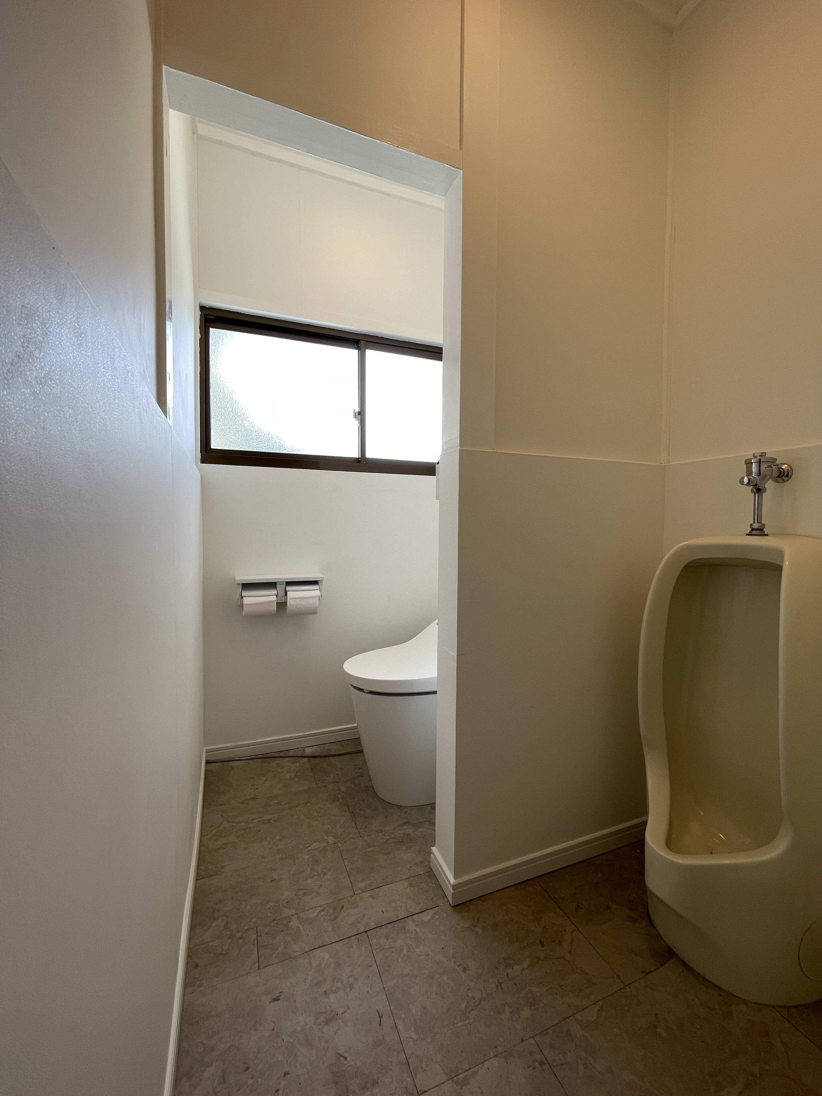 A small, narrow bathroom with a toilet, urinal, and a window.