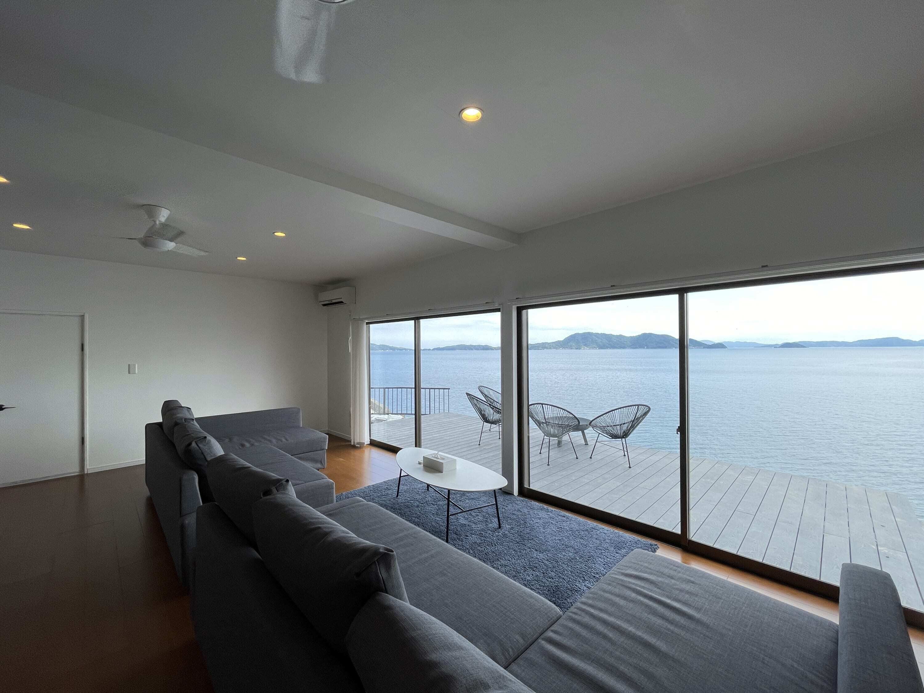 A modern living room with a large gray sofa, a small round table, and a view of the sea through large windows.