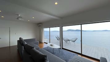A modern living room with a large gray sofa, a small round table, and a view of the sea through large windows.