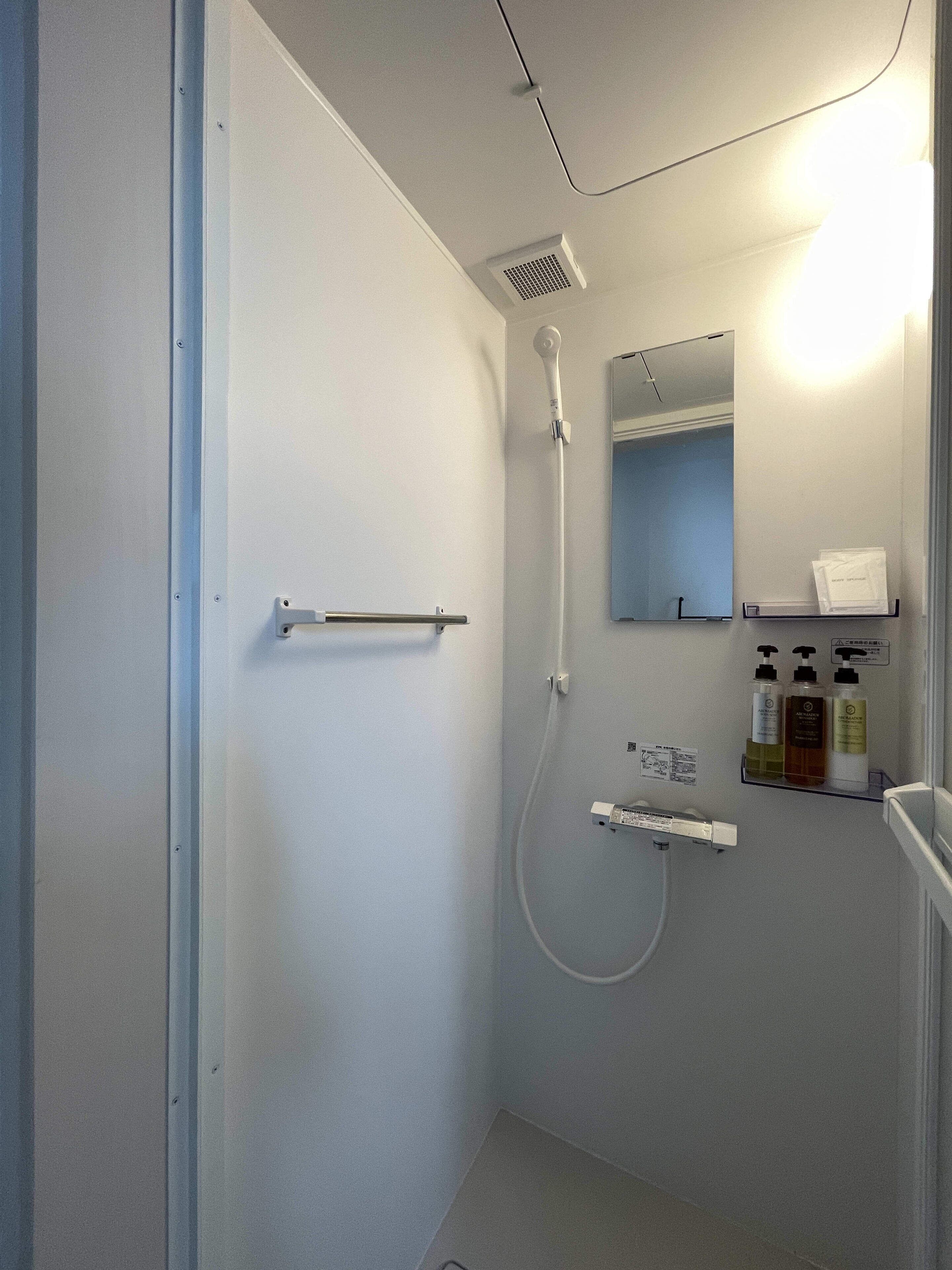 A small, modern bathroom with a shower, a towel rack, a mirror, and a shelf with toiletries.
