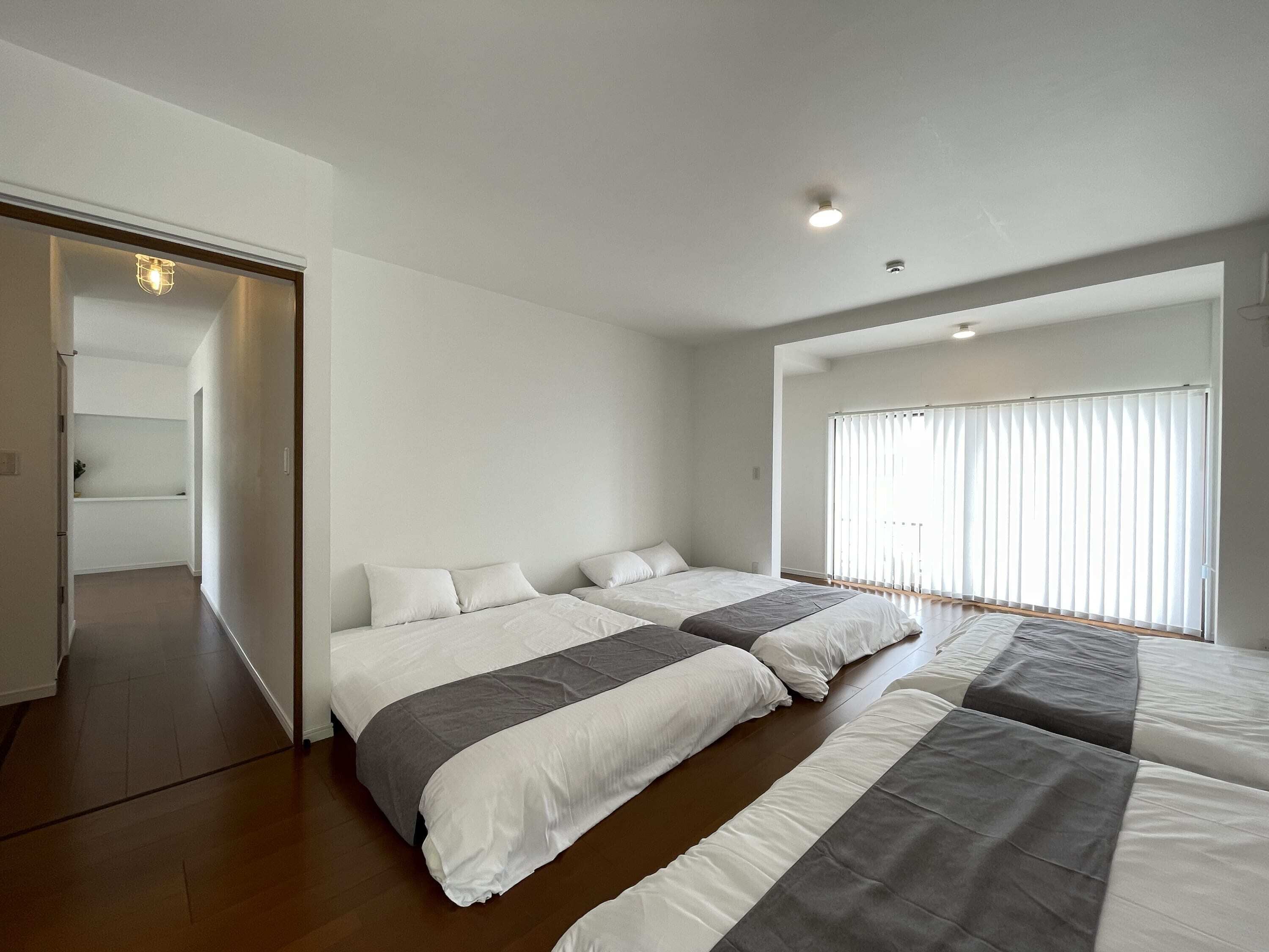 A modern bedroom with two beds, a walk-in closet, and a large window with blinds.