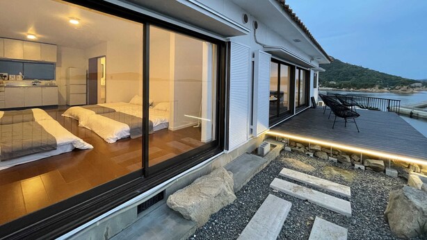 Une chambre d’hôtel moderne dotée d’une grande porte-fenêtre coulissante donnant sur un balcon aménagé avec des sièges d’extérieur.