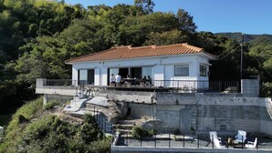 Un bâtiment blanc avec un toit recouvert de tuiles rouges, un balcon et une vue sur une colline boisée.