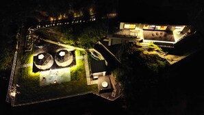 Vue aérienne d’une propriété comprenant un vaste espace ouvert, deux grandes structures sphériques et un bâtiment doté de nombreuses fenêtres.