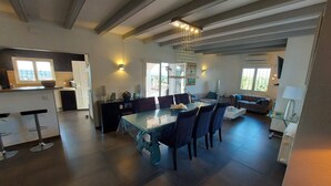 Un vaste espace de vie comprenant un coin repas avec une table, des canapés et une cuisine dotée d’une grande fenêtre.