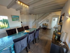 A dining area with a long table, dark chairs, and a hanging light fixture. There is a staircase in the background leading to another level. - Modern villa with stunning views and swimming pool. (L'Escala)