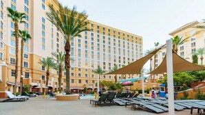 A hotel courtyard with a swimming pool, lounge chairs, palm trees, and a large building in the background. - Spend Christmas in this luxurious condo in Vegas! (Las Vegas)