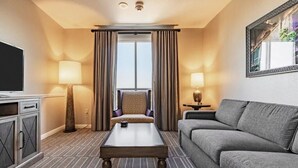 A hotel room with a sofa, a coffee table, a TV, a lamp, and a view through a window with curtains. - Spend Christmas in this luxurious condo in Vegas! (Las Vegas)